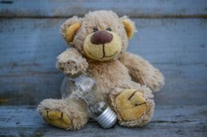 Adorable teddy bear holding a clear glass light bulb on a wooden surface.