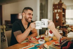 A joyful couple toasting with customized mugs during breakfast at home.